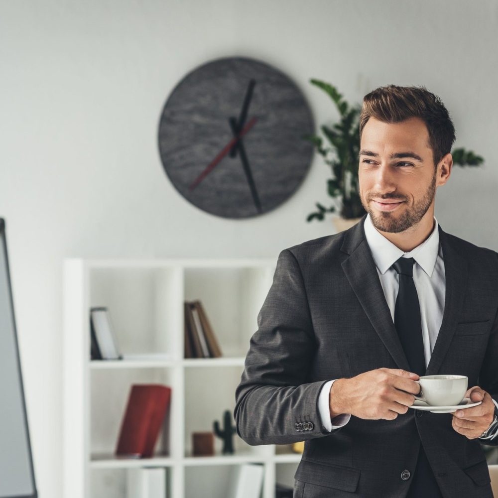 happy-young-businessman-with-cup-of-coffee-at-offi-JB7JNZ8.jpg